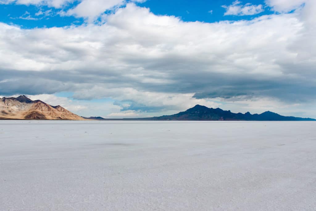 Bonneville Salt Flats near Salt Lake City Utah. Other worldy landscape with large expanse of white salt covered ground with distant mountains and a cloudy blue sky. Bonneville salt flats is a great day trip from Salt Lake City to take.