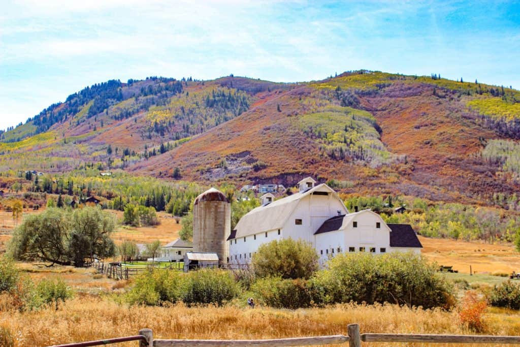 McPolin Barn in Park City, Utah nestled in the foothills of mountains covered in fall foliage and surrounded by golden wheat grass. A great stop on a day trip to Park City.