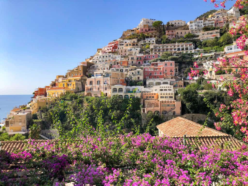 Stunning view of Positano surrounded by blooming flowers. Deciding to visit the Amalfi Coast or Cinque Terre is a hard choice but this guide will help you choose.