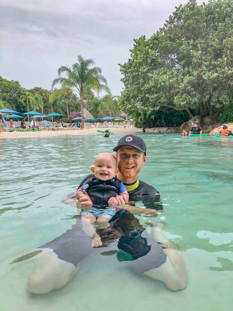 Father and son playing in the warm waters of serenity bay. A day at discovery cove with a baby is so fun! Babies at discovery cove can participate in all the free activities included in your admission. Your young babies and toddlers can enjoy playing in the sand, swimming in the shallows and snacking all day long. The animal free waterways are plenty warm for infants who visit discovery cove. make sure you visit this all inclusive day resort in Orlando during your next visit!