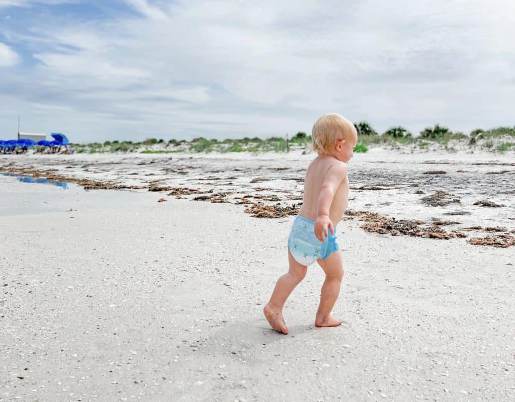 Young toddler or baby playing on the beach in a swim diaper.