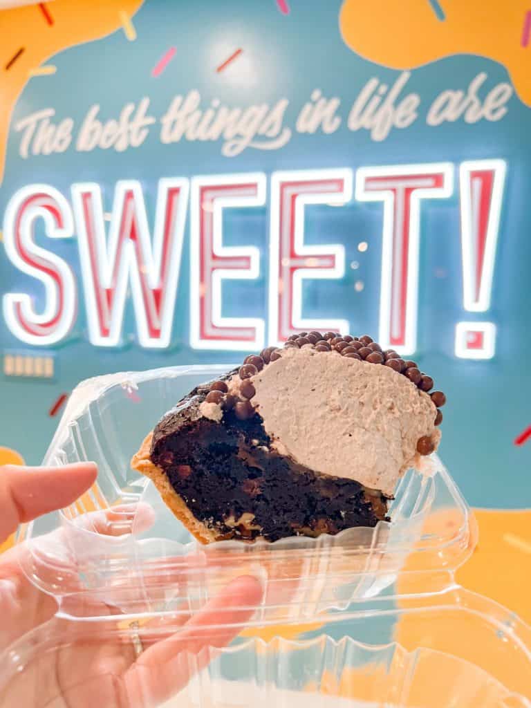 A large piece of pie from Fireman Derek's Bake Shop in front of a mural that says "the best things in life are sweet".