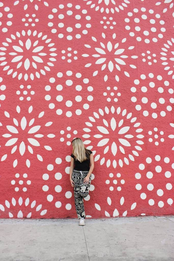 A bright pink and white mural in the Wynwood neighborhood of Miami with a woman posed in front.