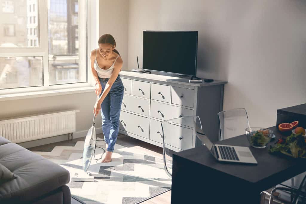 a Woman vacuuming as she cleans her apartment before leaving on vacation. This is an important step on the leaving home checklist in order to come back to a nice home after a fun vacation.