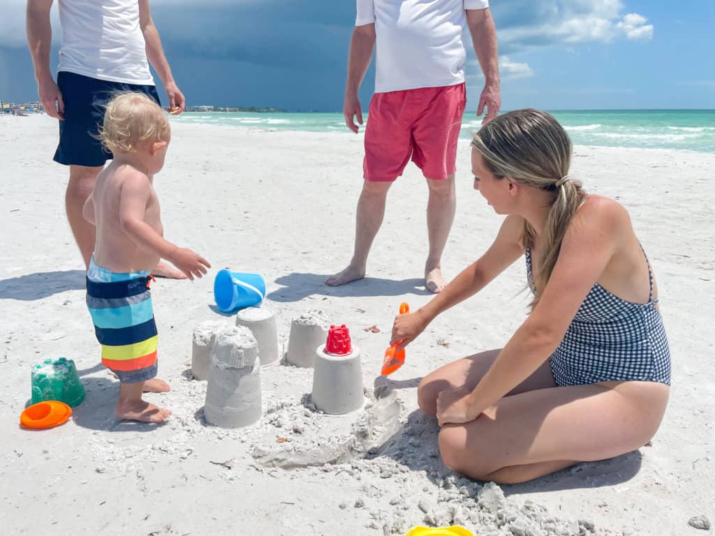 Mom and baby in a swim diaper building a sand castle at the beach. Using swim diapers at the beach allows for hours of comfortable worry free play. Whether you decide to use a disposable swim diaper or a reusable swim diaper, they are a must when babies are around water.