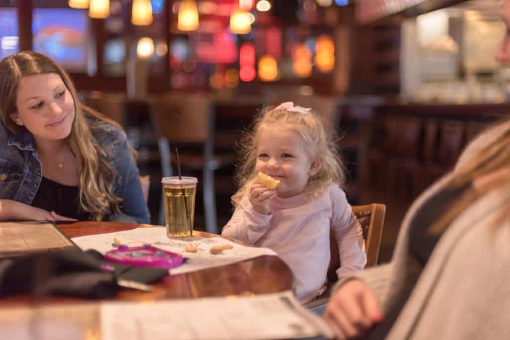 A cute young girl eating out at a restaurant with her family. Take advantage of promo days when kids eat free in Tampa.