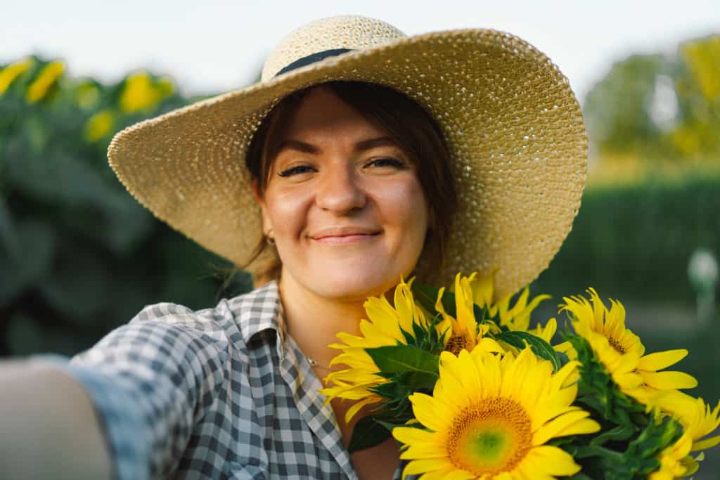 Woman in a straw hat holding a bunch of sunflowers and smiling.