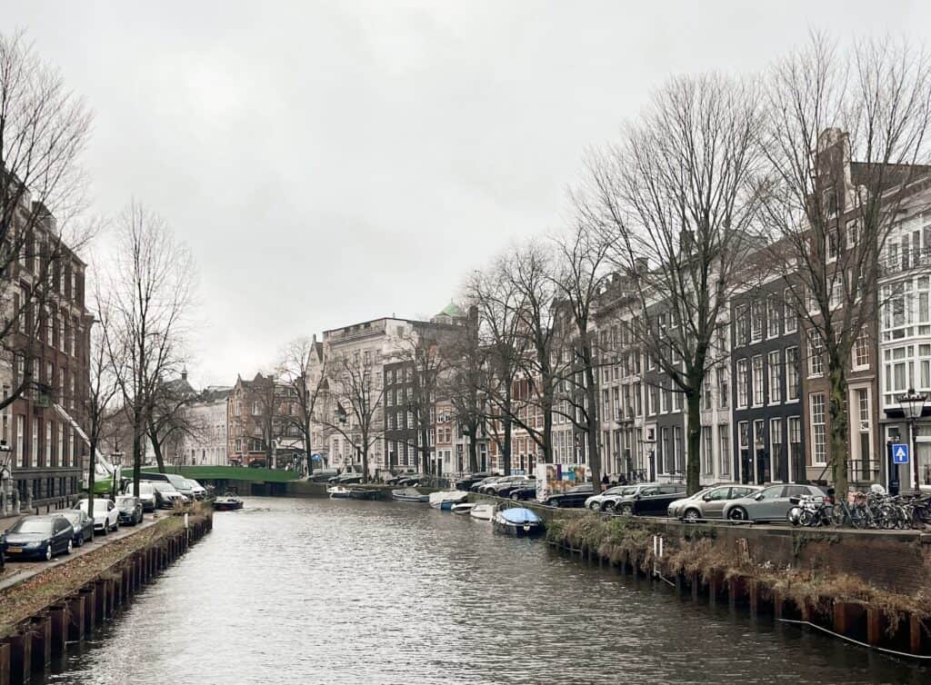 One of Amsterdams many canals lined by boats and cars and brownstone houses on a cold winters day. You can see much of Amsterdams central downtown area during a long layover in Amsterdam if you leave the airport.