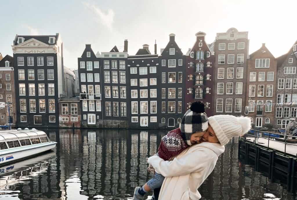 Traveling to Amsterdam with a toddler can be so much fun. This mom and toddler are enjoying the view of the houses along the canal during a layover in Amsterdam.