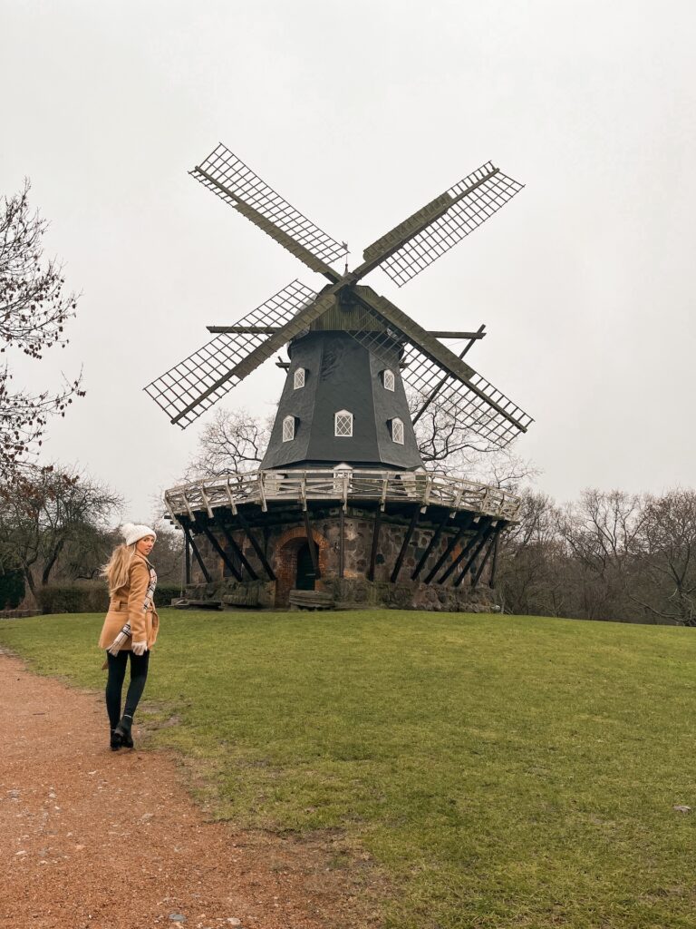 A woman walking on the path leading to a large old wooden windmill.