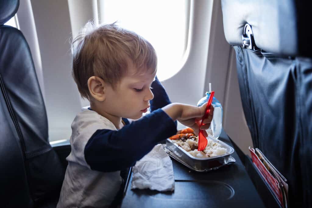 Young boy eating an airplane meal on a plane during a flight