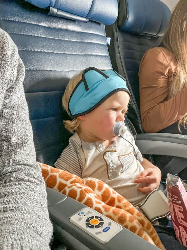 Young boy on a flight using his pacifier at takeoff to help his ears pop. He also has a bag of snacks in his lap.