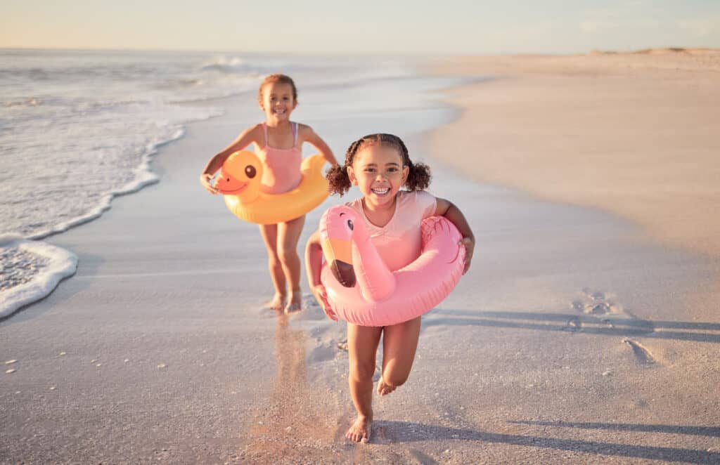 Two small children playing together on the beach during their family trip. The best age to travel with kids is as early as 3-5 years old.
