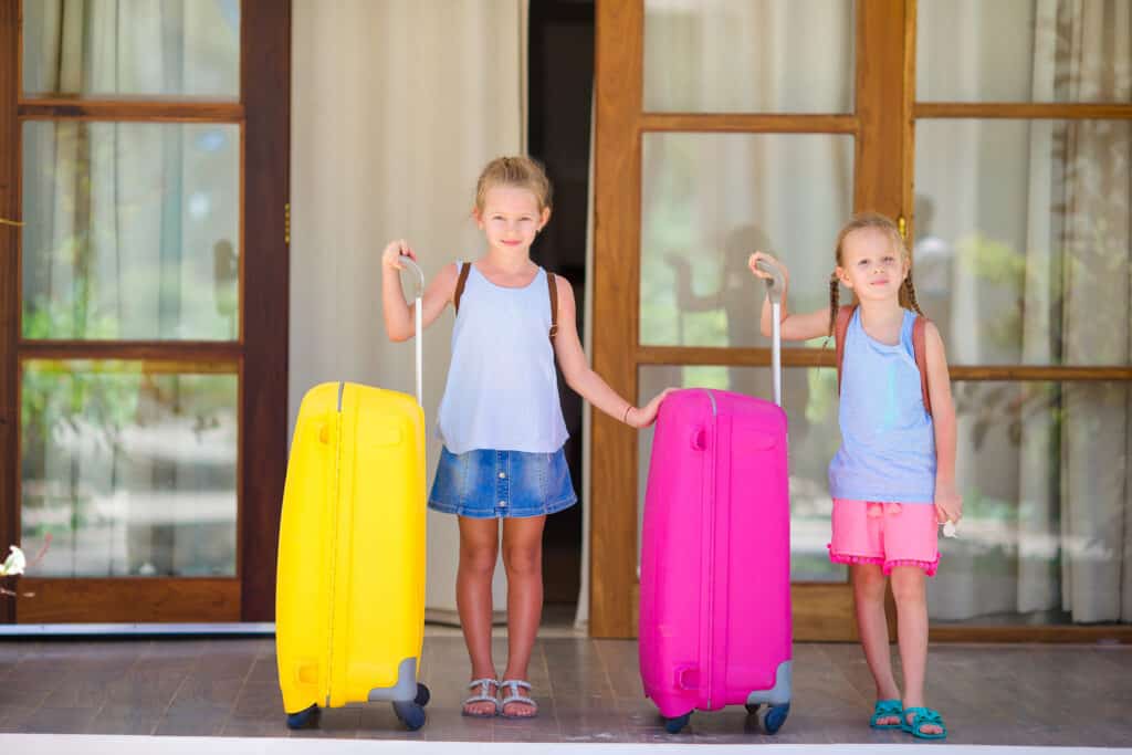 Two girls with their suitcases ready to explore with their family. The best age to travel with kids is when everyone is excited.