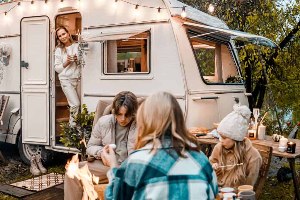 A mom watching her teenagers enjoy making s'mores together outside their camper. Teenagers can be in the best age to travel with kids. Traveling with teens is wonderful family bonding time.