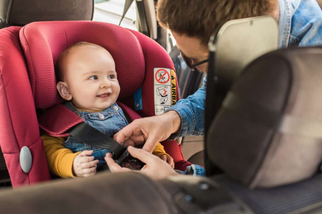 a father buckling his son into his car seat after a road trip break with a diaper change and stretch break.