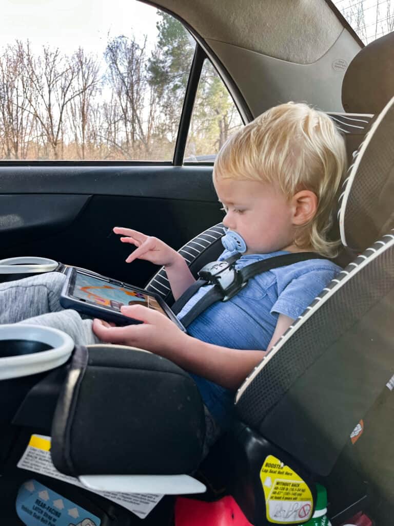 toddler on a road trip playing a game on his tablet to pass the time.