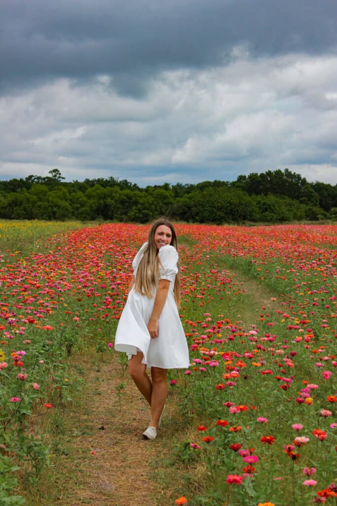 A woman in a white dress twirling in a field of bright pink, red and orange flowers