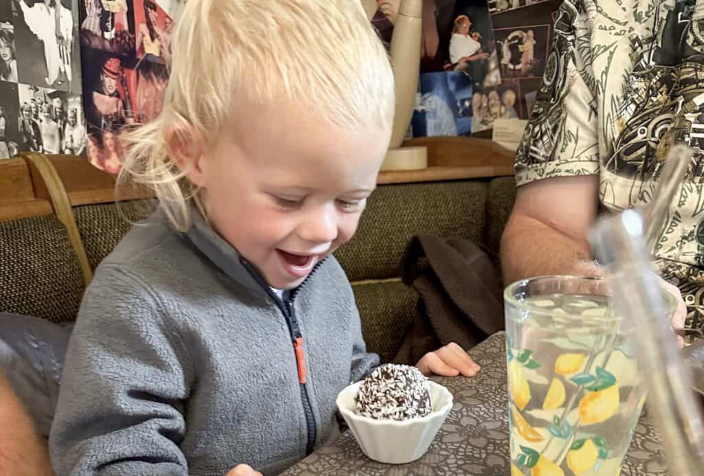 A young boy looking excitedly at a chocolate ball. A swedish treat made from oats, cocoa powder and coconut.