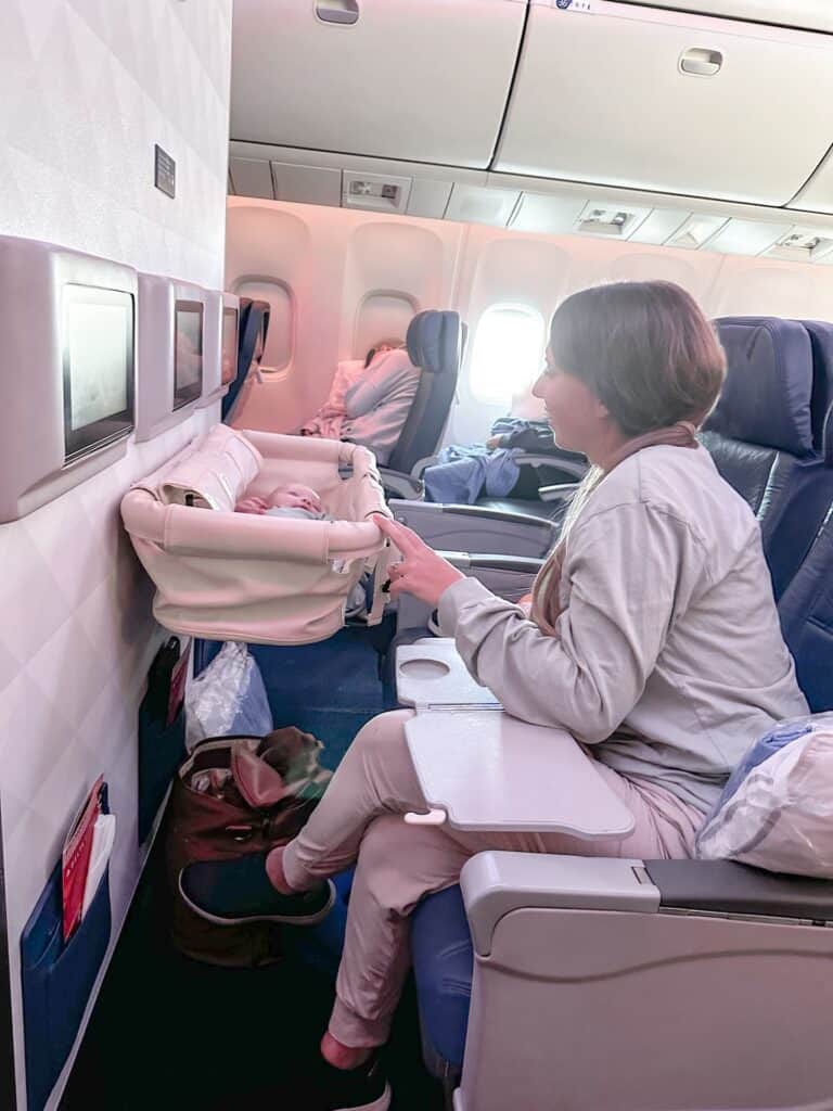 A mother peering into an airplane bassinet at her small baby.