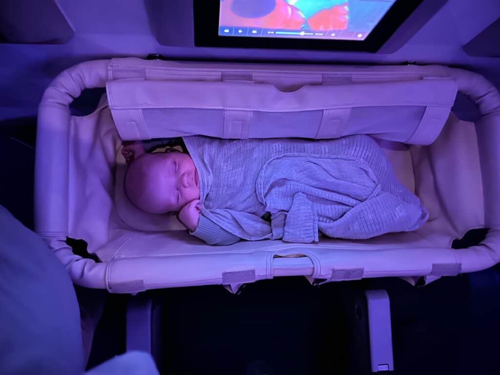 a small baby peacefully asleep in an airplane bassinet. It is a very comfortable way for babies to travel.