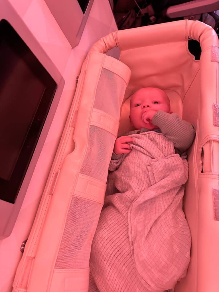 A small baby awake and happy in an airplane bassinet mid flight.